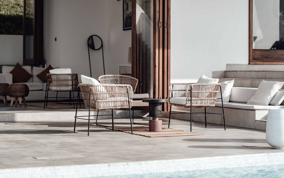 Wicker lounge chairs with white cushions on a stone patio beside a pool.