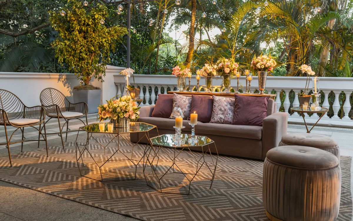 An outdoor lounge with a gray sofa, patterned rug, glass coffee tables and chairs beside a balustrade.