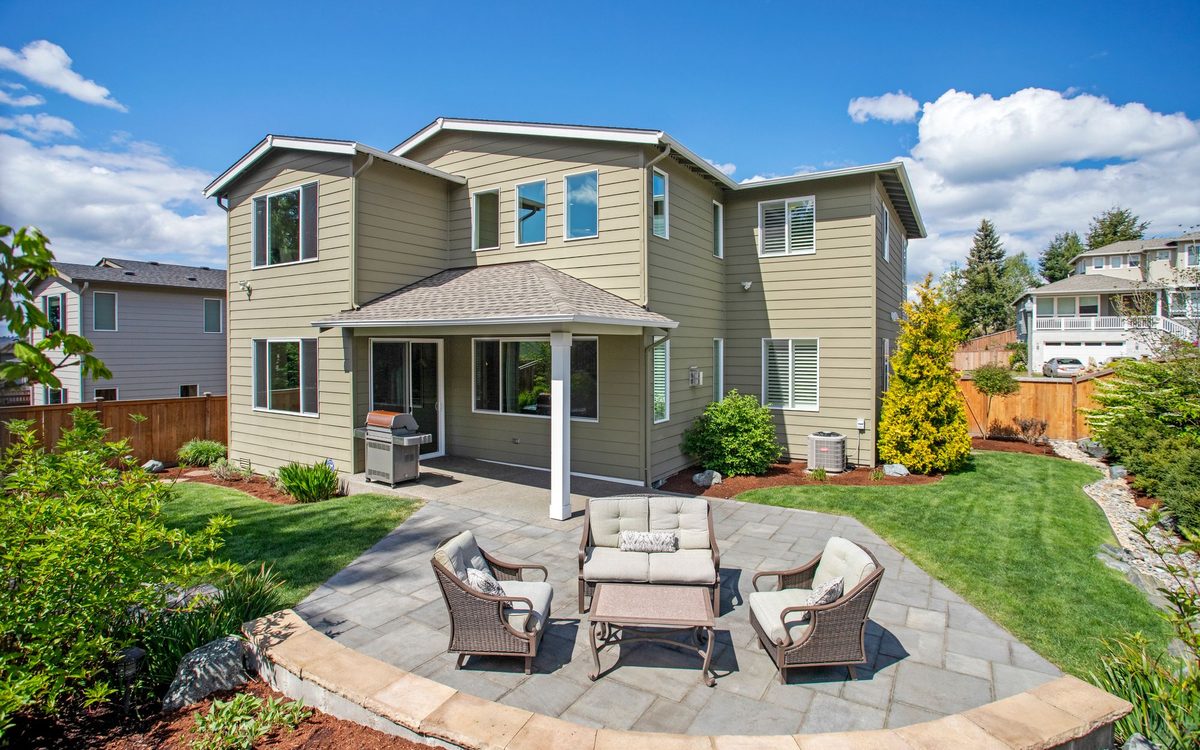 Wicker patio sofa, two armchairs and a coffee table on a stone patio behind a suburban house.