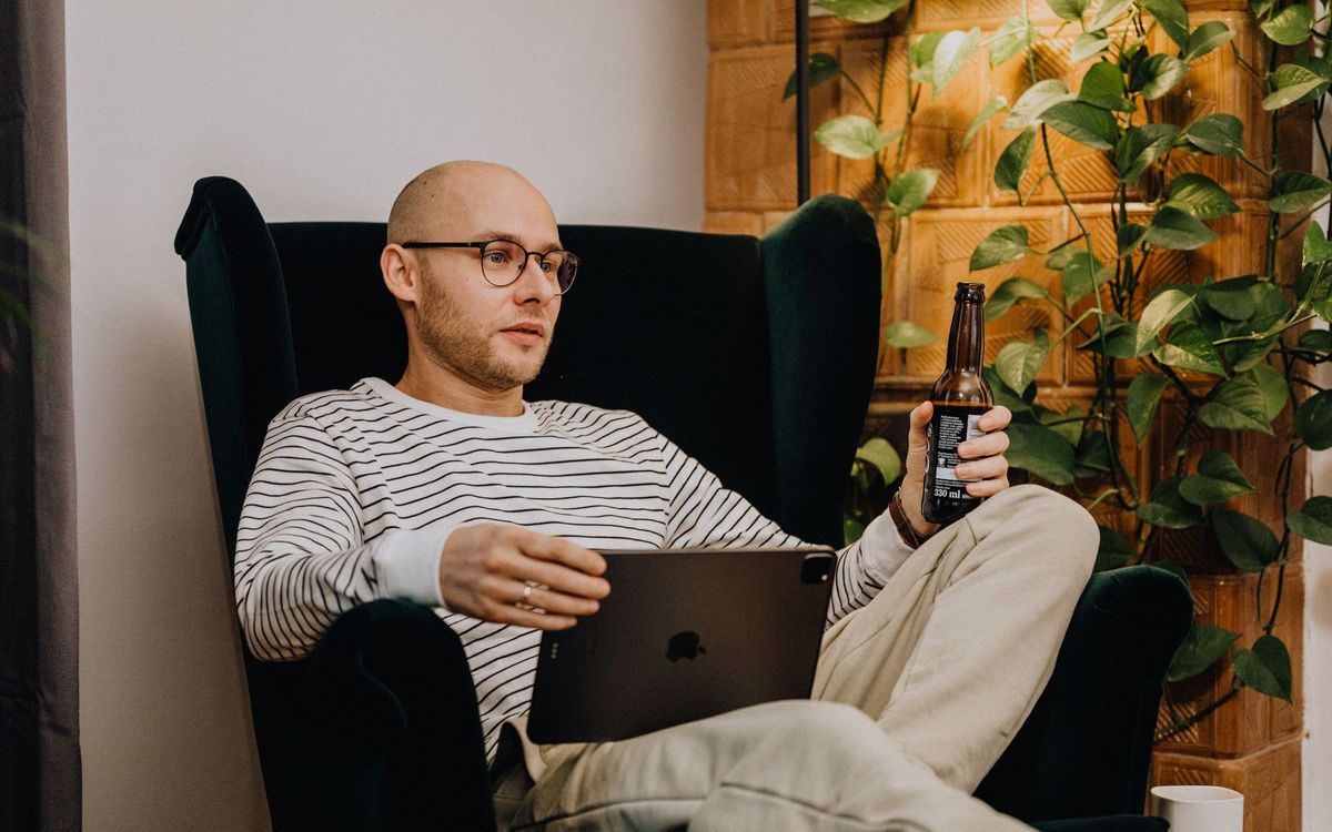 Adult man sitting in an armchair with a tablet, surrounded by plants for a relaxed atmosphere.