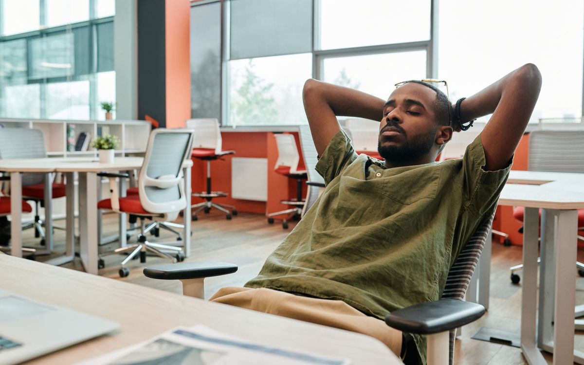 Young man resting in an office chair, eyes closed, in a modern workspace. Captured with a DSLR camera.
