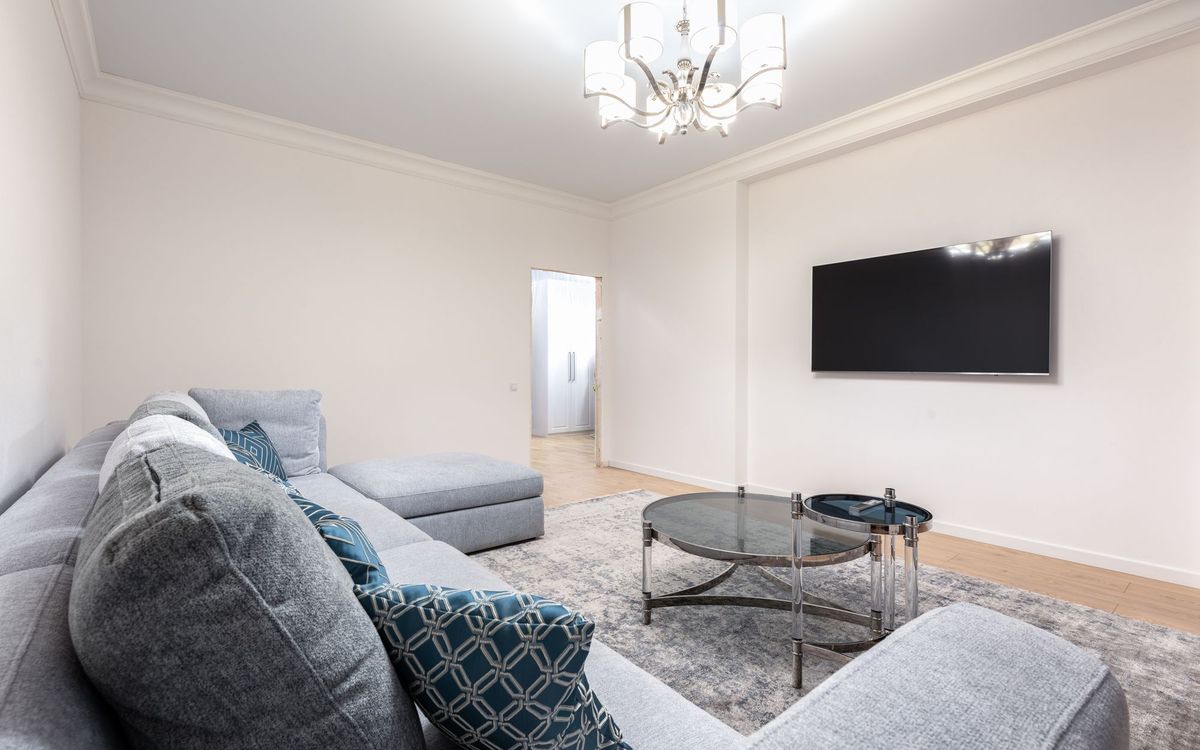 Contemporary room interior with couch and TV against tables under a chandelier in a house.