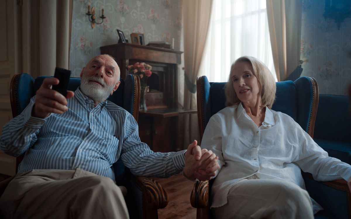 Senior couple watching TV in matching wingback recliner armchairs in a home living room.