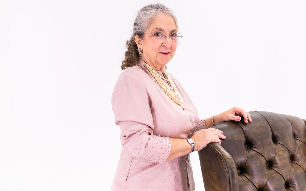 Woman in a pink jacket standing beside a leather chair indoors