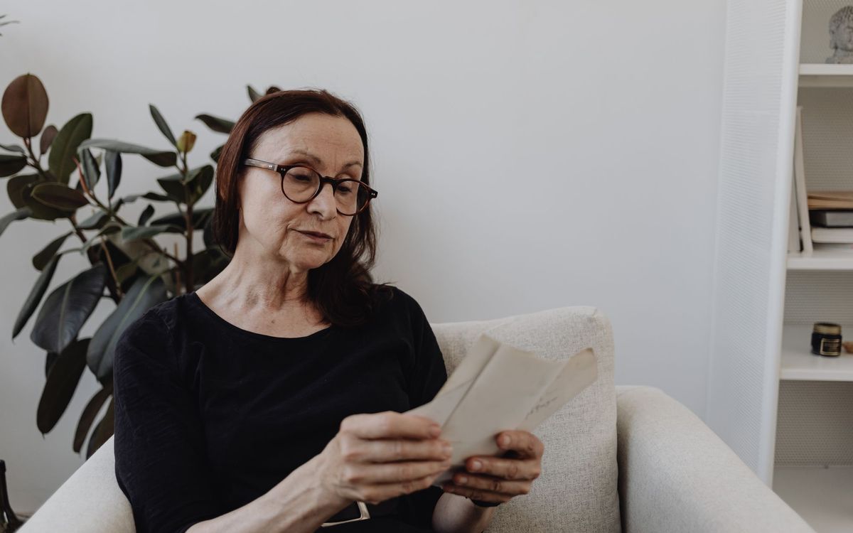 Senior woman sitting in a cream armchair indoors beside a plant