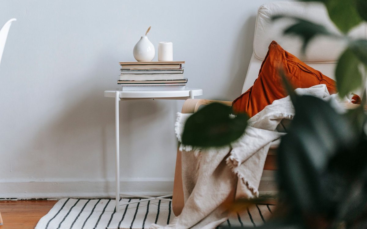 Light room with an armchair, cushion and plaid beside a small table with a stack of books