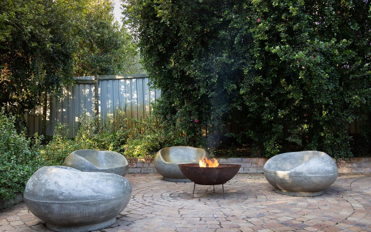 Backyard patio with three round stone chairs arranged around a small bowl-style fire pit on pavers