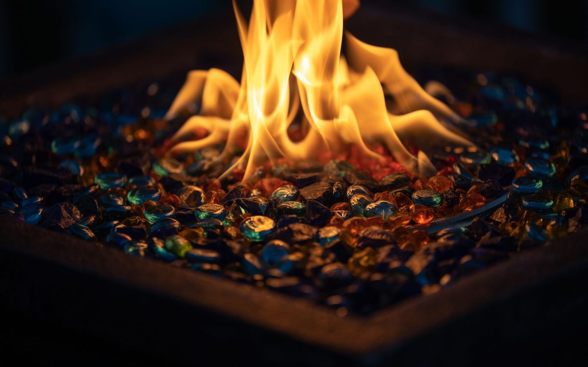 Close-up of flames rising over colorful fire glass in a gas fire pit burner pan