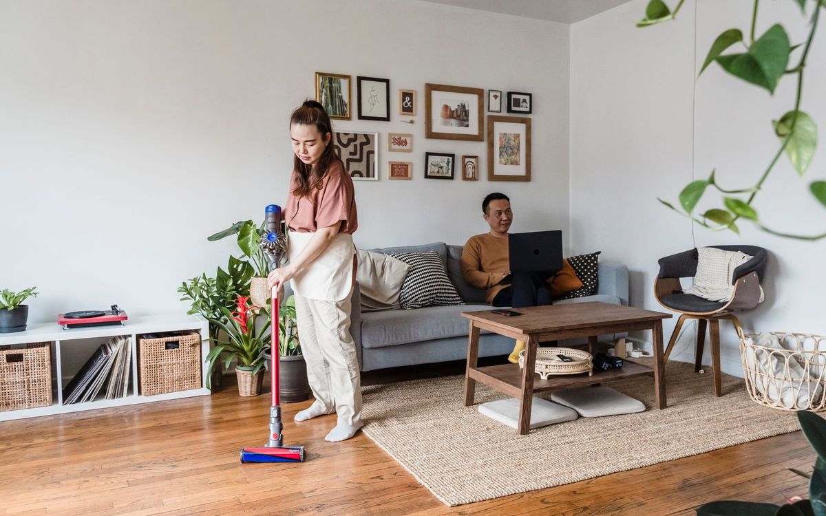 Woman vacuuming while man works remotely on laptop in cozy living room