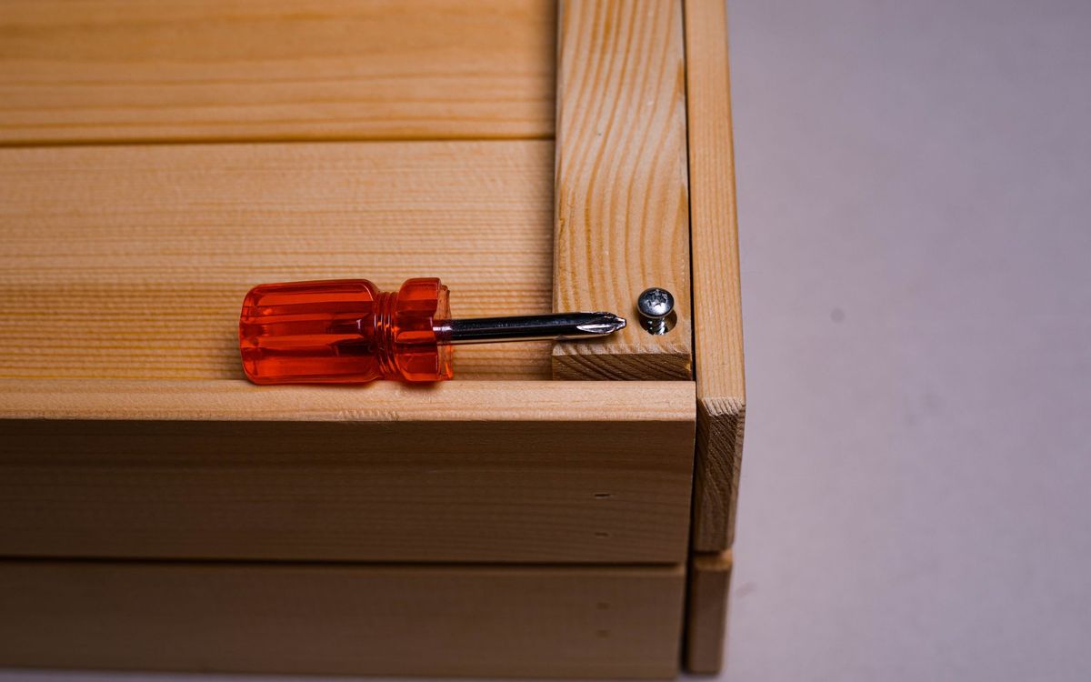 Orange-handled screwdriver lying on a wooden box beside a loose screw