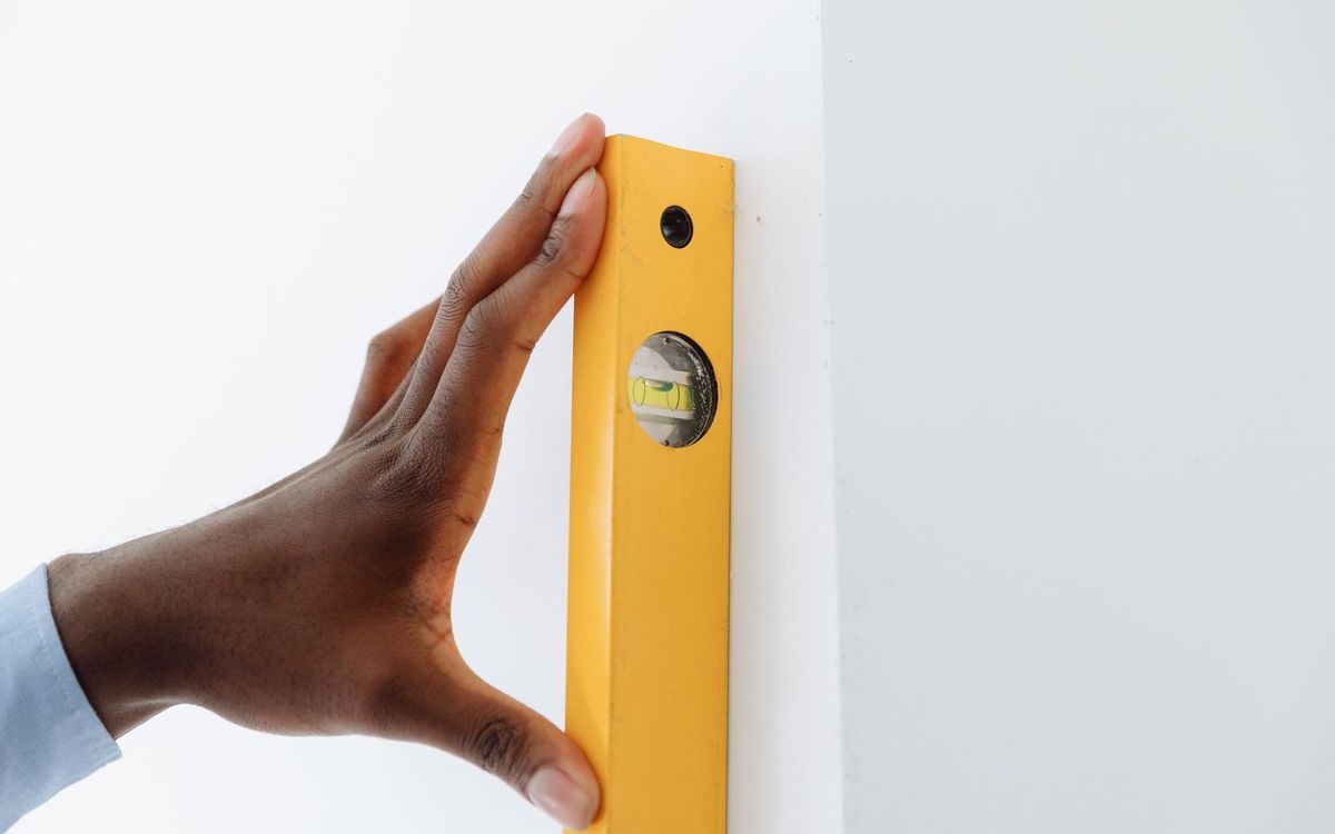 A close-up of a hand using a yellow level tool against a white wall to ensure vertical alignment