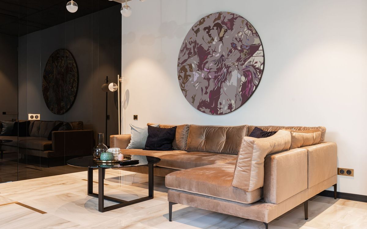 Large round wall art hung high on a living room wall above a velvet corner sofa