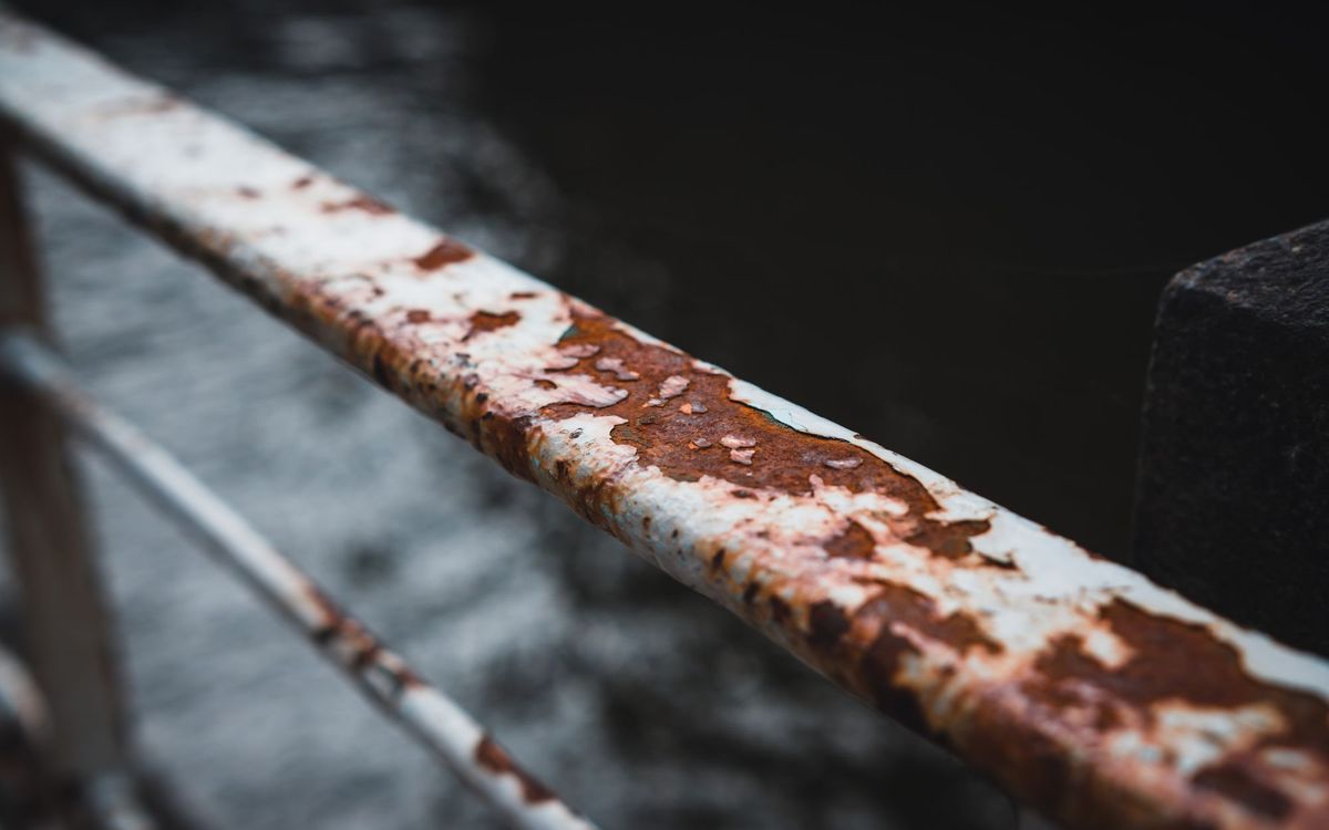 Chipped white paint and orange rust on a metal railing, the way rust starts at a chip