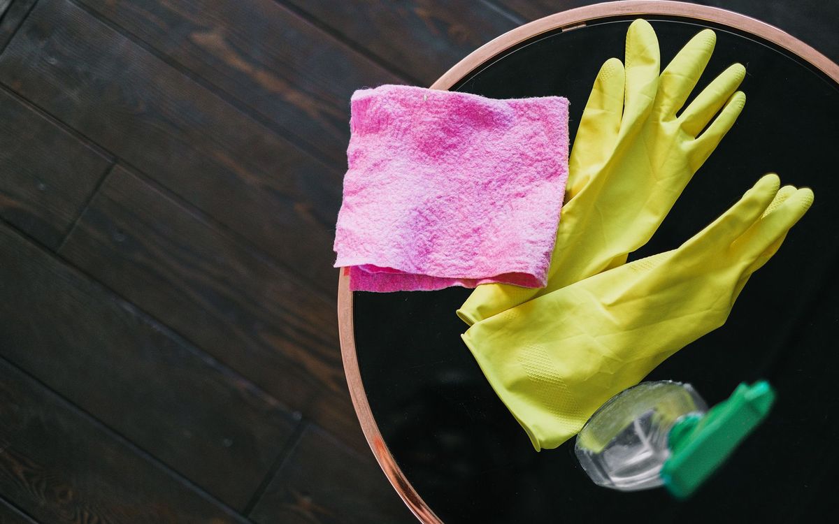 Yellow cleaning gloves, a pink cloth and a spray bottle on a round table