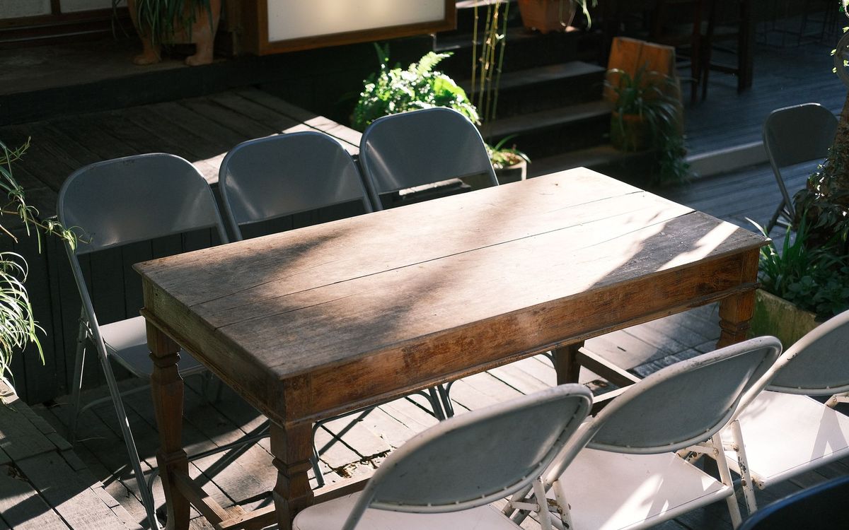 Outdoor patio scene with wooden table and folding chairs surrounded by greenery