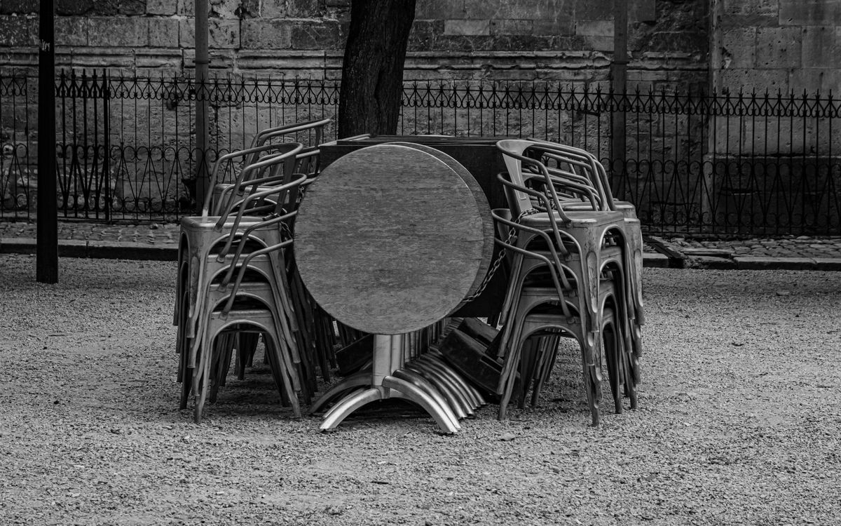 Metal chairs and a round folding table stacked together outdoors, in black and white
