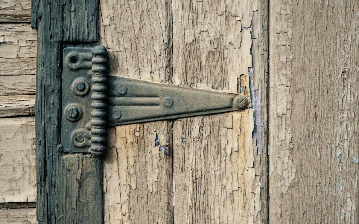 Old iron strap hinge on a weathered wooden door, the kind of metal pivot that benefits from a little lubricant