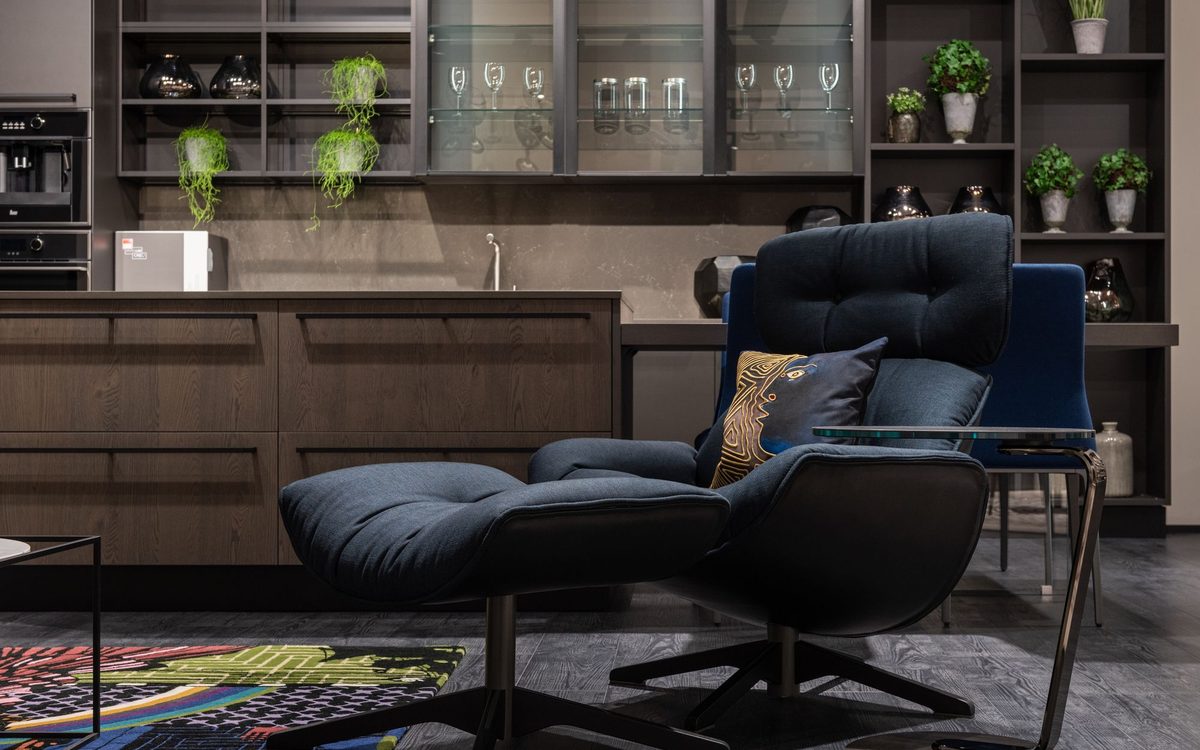 Dark blue upholstered swivel lounge chair with a matching ottoman and a patterned cushion in a modern open kitchen and living area