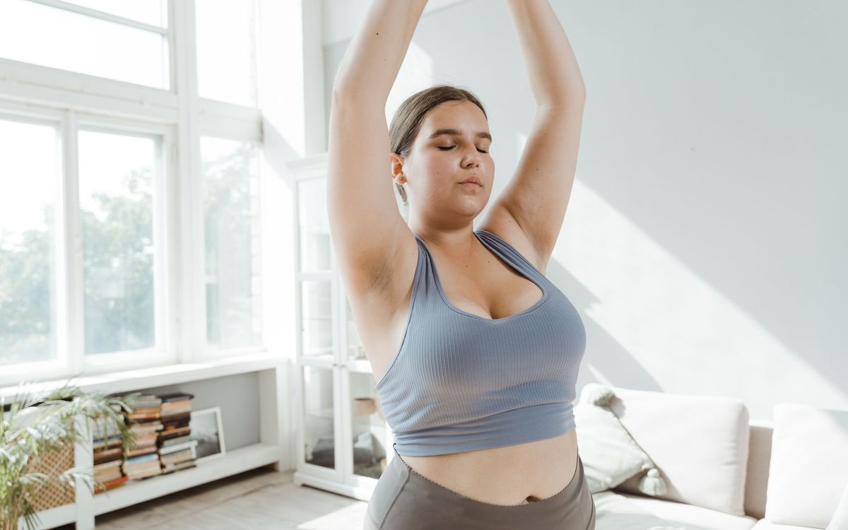 Woman stretching her arms overhead in a living room, a gentle wellness routine to pair with a massage chair session