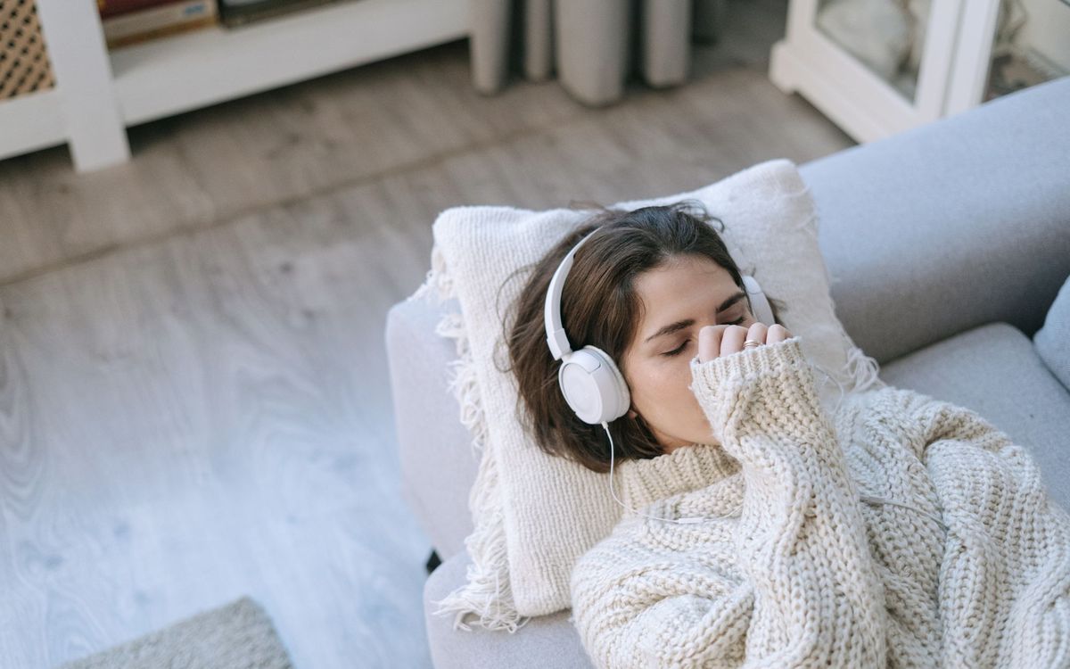 Woman in cozy sweater with headphones relaxing on a sofa, the kind of rest that follows a massage chair session