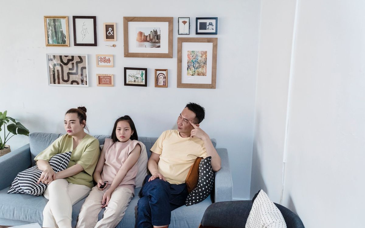 A family of three sitting on a sofa in a modern living room with a gallery wall.