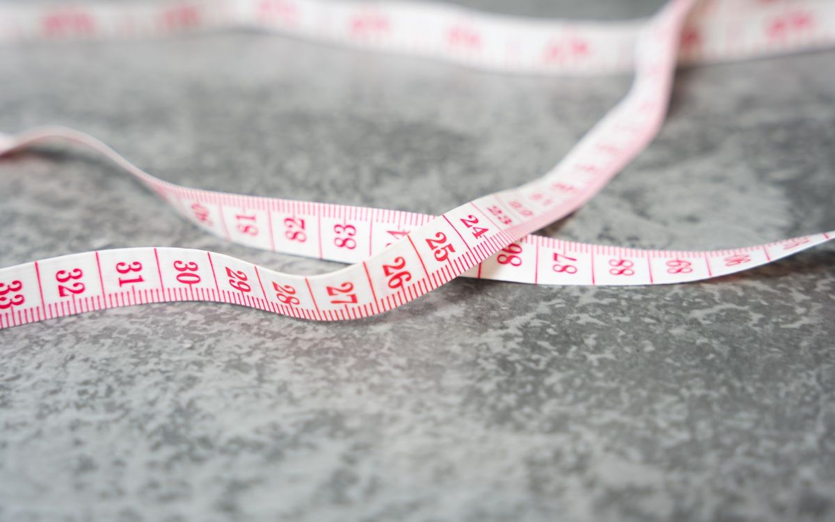 A detailed close-up of a measuring tape with pink numbers on a gray textured surface.