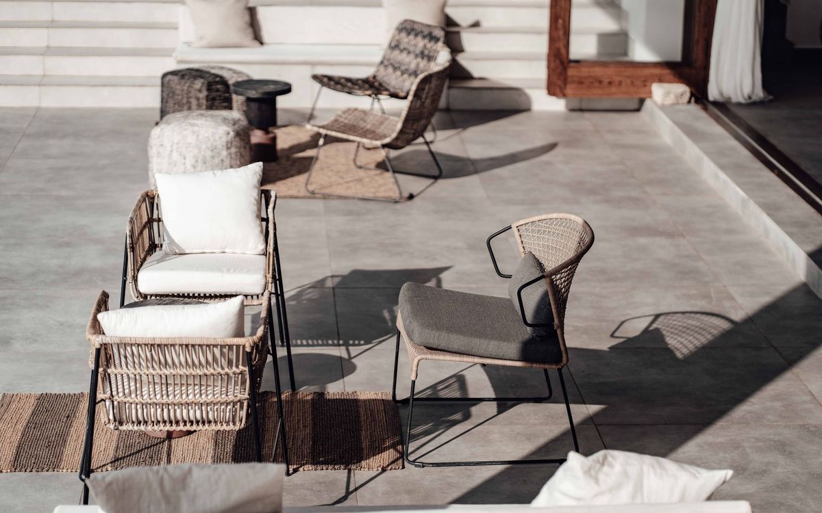 Woven wicker lounge chairs with white and gray cushions and a jute rug on a stone-tiled patio