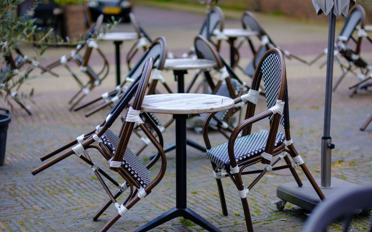 Woven bistro chairs around small round tables on a cobbled outdoor terrace