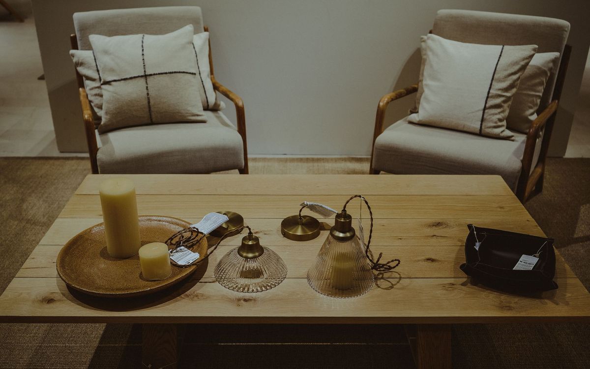 Two upholstered armchairs with cushions beside a wooden coffee table with candles and lamps