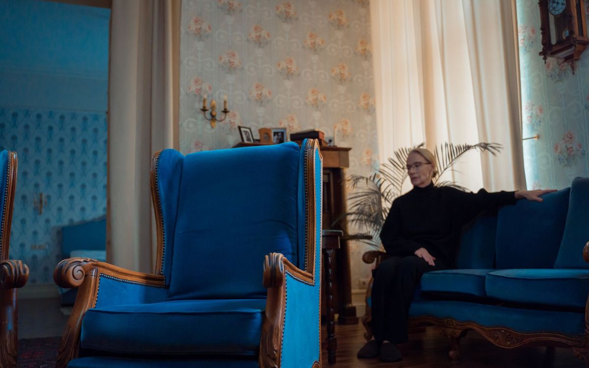 Blue wingback armchair and a woman seated on a sofa in a traditional living room