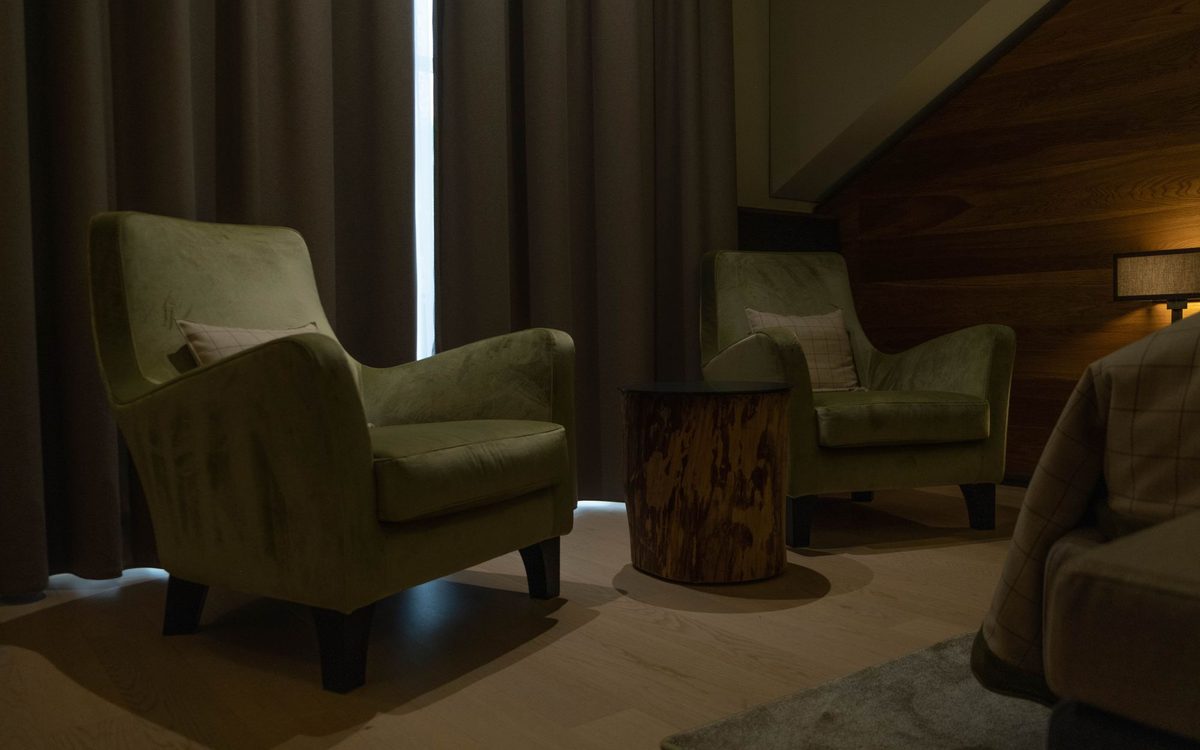 Two green armchairs in a dimly lit room beside a wooden side table