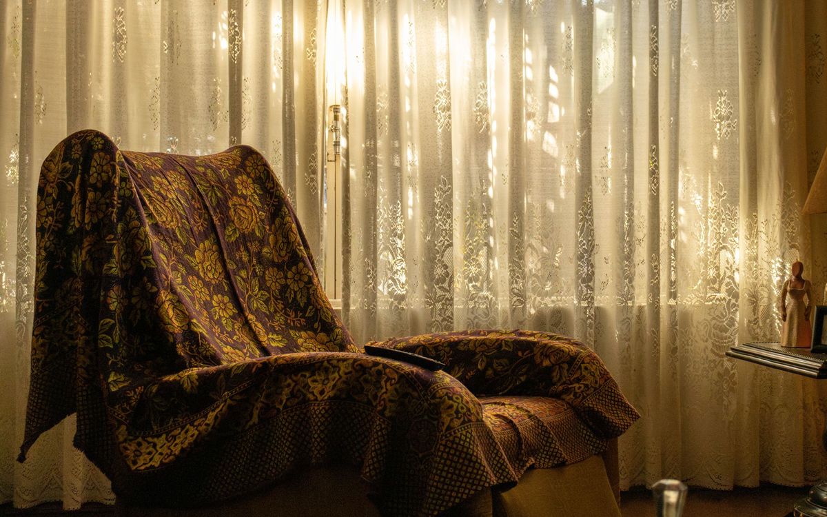 Armchair draped with a floral throw beside a lace-curtained window