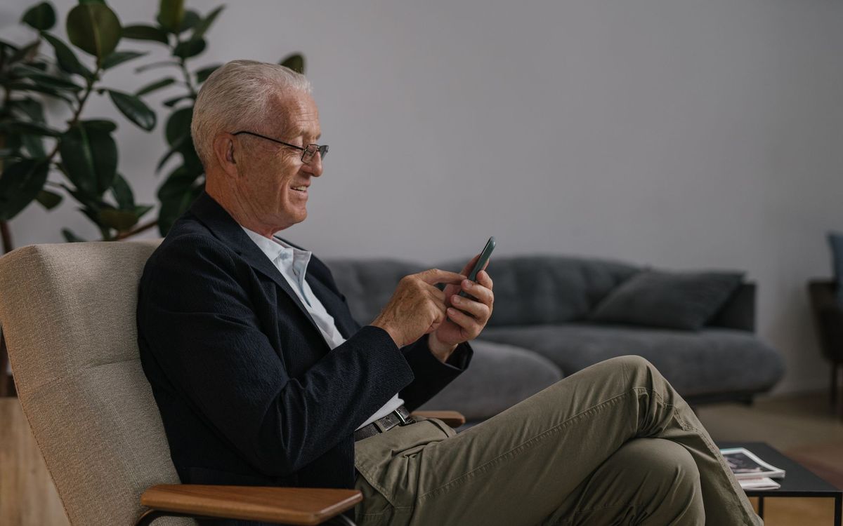 Older man in a smart jacket sitting back in an upholstered chair in a living room