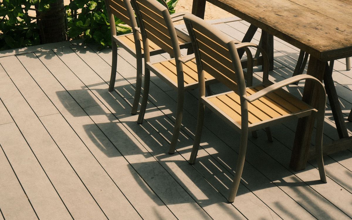 Slatted-seat outdoor furniture: stackable armchairs beside a wood dining table on a sunny gray deck.