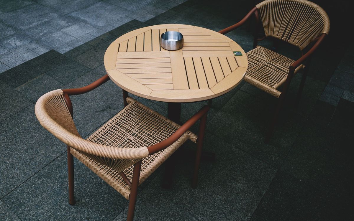 Round slatted outdoor table with two woven rope-seat chairs on a stone-paved patio.