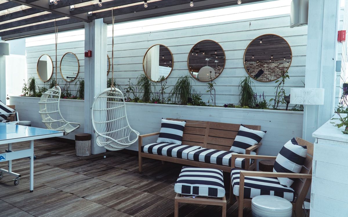 Wooden outdoor bench and armchair with striped cushions under a pergola beside two white hanging chairs.