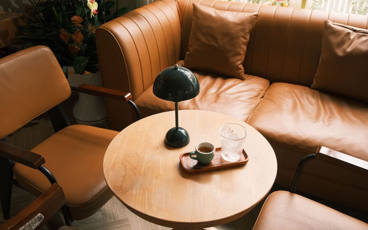 A warm living room corner with tan leather armchairs, a leather sofa and a small round table with a green lamp